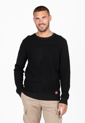Schwarzer gestrickter Pullover mit langen Ärmeln, Rundhalsausschnitt, geripptem Saum und einem kleinen braunen Logo-Patch an der unteren linken Ecke.