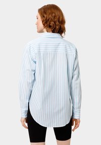 Camicia a righe blu chiaro con maniche lunghe, orlo arrotondato, polsini abbottonati e una sottile trama. La vista posteriore mostra un motivo a righe verticali.