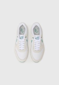 Białe i beżowe sneakersy Nike Air z miętowym akcentem, z gładką tekstylną cholewką, sznurowanym zapięciem oraz widoczną amortyzującą podeszwą.