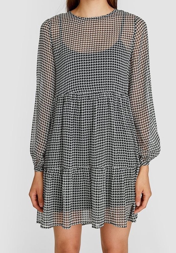 Vestido de houndstooth en blanco y negro con transparencias, de manga larga, escote redondo y falda con volantes, que presenta una textura ligera.