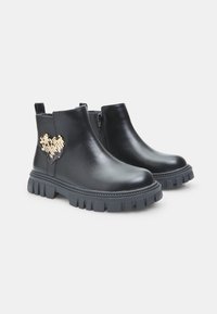 Botas de letra negra hasta el tobillo con un acabado suave, que presentan un detalle en forma de corazón de lentejuelas doradas y suelas de goma resistentes. Cierre con cremallera en el lateral.