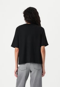 Black short-sleeved top with a relaxed fit, made of soft fabric. Features a round neckline and smooth texture, paired with light gray jeans.
