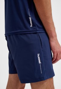 Marina blå atletiska shorts och matchande topp, tillverkade av ett mjukt tyg med en smal passform. Har en vit "hummel"-logotyp på sidan.