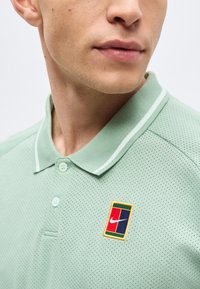 Άνδρας που φοράει ανοιχτό πράσινο διάτρητο πόλο με γιακά, με μικρό ορθογώνιο λάβαρο λογότυπου Nike στο στήθος.