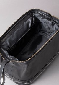 Black leather cosmetic bag with a zippered closure, smooth texture, interior mesh pocket, and contrasting white stitching along the base.
