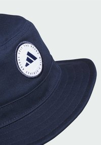 Marineblauwe bucket hat gemaakt van duurzaam materiaal, voorzien van een ronde witte patch met een logo en drie gestreepte details.