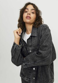 Zwarte denimjack met een relaxed fit, zichtbare stiksels, grote knopen en een omgeslagen kraag. De stof heeft een vervaagde textuur.