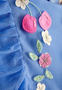 Blauer Mesh-Stoff mit gerafften Kanten, verziert mit rosa Kirschen und Blumen, ergänzt durch gestickte Blätter und silberne Akzente.