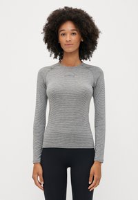 Maglietta sportiva grigia a maniche lunghe con un motivo texturizzato, design aderente e maniche raglan. Piccolo logo sul petto. Abbinata a pantaloni neri.