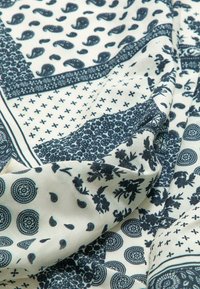 Bomuldsstof med en creme farvet baggrund, der har indviklede mørkeblå mønstre, herunder paisleys, blomster og geometriske designs.