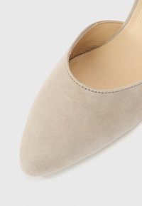 Escarpin en daim beige avec un bout pointu et des côtés coupés bas, présentant une texture lisse et des détails de coutures minimaux.