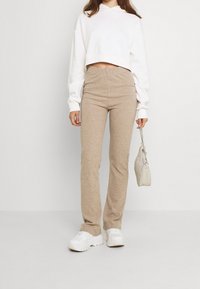 Béžové žebrované pletené kalhoty ve slim střihu, doplněné o bílou krátkou mikinu s kapucí a bílé robustní tenisky. Světle béžová kabelka s řetízkovým popruhem.