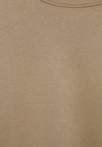 Gros plan d'un tissu beige doux avec une texture fine en maille et un col rond, suggérant un vêtement en coton ou en tricot.