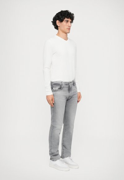 Herren Langarm-weißer Hemd, hellgraue Jeans, weiße Sneaker. Slim Fit mit einer glatten Textur, vor einem schlichten Hintergrund präsentiert.