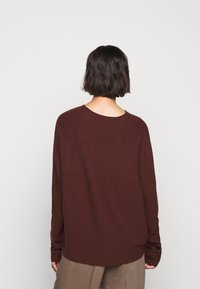 Brauner Strickpullover mit leicht abgerundetem Ausschnitt, überschnittenen Schultern und langen Ärmeln. Verfügt über eine lockere Passform und einen gerippten Saum.