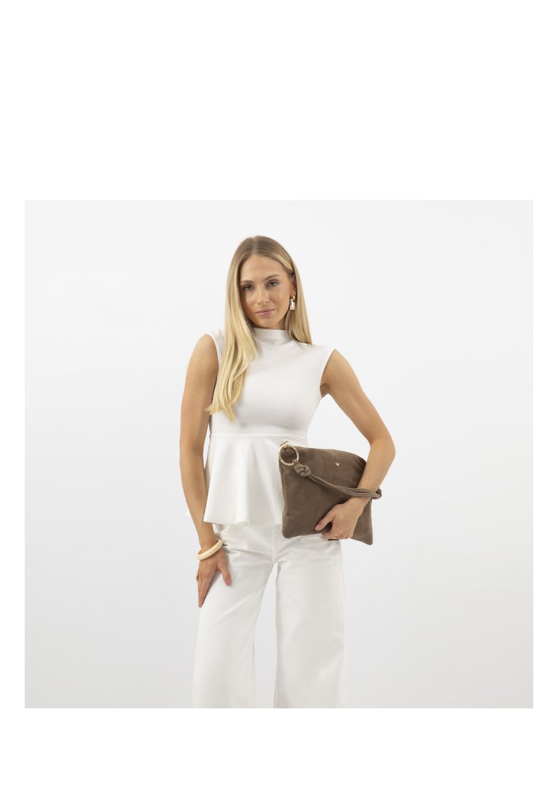 Femme aux longs cheveux blonds porte un top blanc sans manches et un pantalon, tenant une grande pochette marron avec une lanière et un détail anneau doré.
