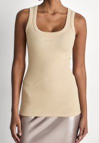 Kvinna som bär en beige ribbad linne med "BOSS"-logotyp präglad på bröstet och en glänsande ljus taupe-kjol.