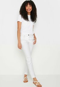 Camiseta blanca de manga corta combinada con vaqueros ajustados blancos y sandalias blancas de tiras. Tejido suave, diseño ajustado, líneas limpias, estilo casual.