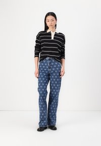 Black and cream striped long-sleeve shirt paired with blue jeans featuring a heart pattern, complemented by black footwear.