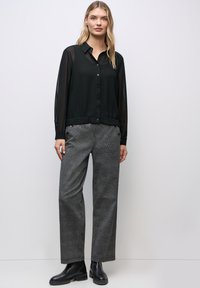 Sort gennemsigtig skjorte med knapper og lange ærmer, parret med grå ternede brede bukser og sorte ankelstøvler.