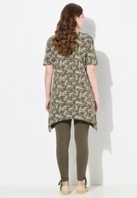 Tunique olive verte avec un motif floral blanc, à manches courtes et un ourlet arrière plus long, associée à des leggings olive et des espadrilles beige.