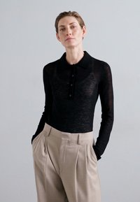 Must have pikkade varrukatega must polo särk struktuurse viimistlusega, viis nööpi eesmisel klapil, kombineeritud kõrge vöökohtadega beežide pükstega.