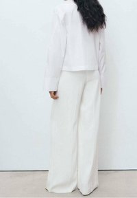 Chemise blanche coupée aux manches longues associée à un pantalon blanc à jambes larges. Tissu lisse, design minimaliste et silhouette épurée.