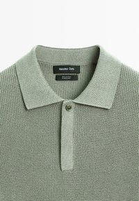 Polo shirt in cotone di colore verde chiaro, con un motivo a nido d'ape testurizzato, colletto classico e chiusura con un solo bottone.