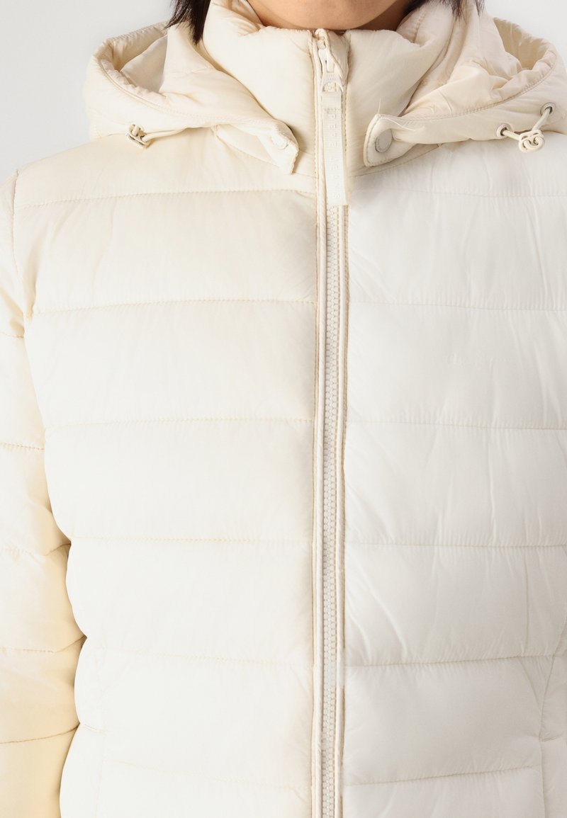 Giacca a vento color crema con zip frontale, cuciture orizzontali e cappuccio. Il materiale sembra liscio e leggermente lucido.