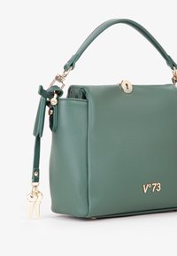 Borsa a tracolla verde in pelle con forma strutturata, accessori in oro, un portachiavi decorativo e manico superiore. Presenta una chiusura a scatto e un logo in rilievo.