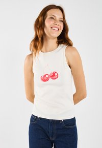 Witte geribbelde tanktop met een rode kers graphic en de tekst "Je bent lief!" in een speelse lettertype. Zachte textuur en getailleerd ontwerp.