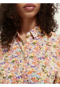Vícebarevná květinová košile s límcem na knoflíky, obsahující oranžové, fialové a zelené odstíny. Lehká tkanina s texturovaným vzorem.