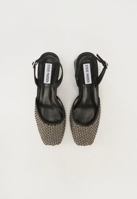 Mustat slingback-korkokengät neliönmuotoisella varvalla, joissa on metalliverkosta valmistettu teksturointi ja sileä nahkasisäpohja. Säädettävä hihna istuvuuden parantamiseksi.
