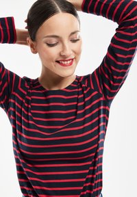 Blå og rød stribet langærmet top med rund halslinje og blød tekstur, der har et asymmetrisk design foran.