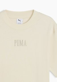 Krémové tričko vyrobené z měkké tkaniny. Kolem krku kulatý výstřih, krátké rukávy, na přední straně s embosovaným nápisem "PUMA" v jemně zelené niti.
