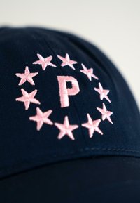 Căciulă navy cu un design circular de stele roz deschis, înconjurând un „P” centrat brodat în aceeași nuanță de roz. Textură fină, din material de bumbac.