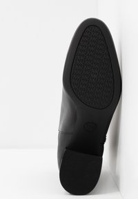 Semelle de chaussure en cuir noir avec une semelle extérieure texturée comportant un motif répété du logo "MK" et un talon bloc bas.