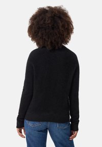 Svart, mjuk stickad tröja med avslappnad passform, ribbade ärmar och rund halsringning, som är kombinerad med blå denimjeans.