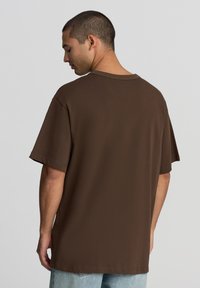 T-shirt marrone oversize con scollatura rotonda e maniche corte, realizzato in tessuto morbido. Il retro presenta un design semplice, senza motivi o dettagli.