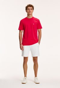 Tricou roșu din bumbac cu guler rotund, detaliu de buzunar pe partea stângă a pieptului. Asortat cu pantaloni scurți albi și adidași. Design simplu și lejer.