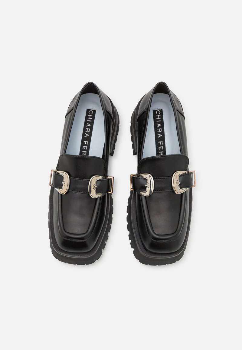 Mocassins en cuir noir avec une semelle épaisse, dotés de deux grandes boucles métalliques et d'un bout arrondi. Intérieur doublé avec branding sur la semelle intérieure.
