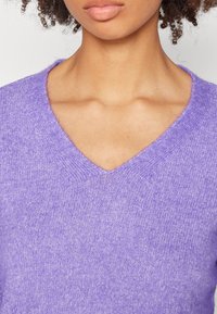 Pull vert de mer en V en tissu doux et texturé. Il présente une coupe légèrement ample et un col côtelé avec des variations subtiles de couleur.