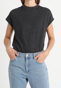 Tmavě šedé tričko s krátkým rukávem vyrobené z měkké tkaniny, s vysokým výstřihem a volným střihem. V kombinaci se světle modrými džíny s vysokým pasem, jemná textura.