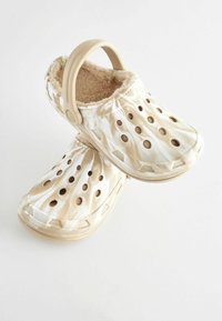 Chaussures : sabots beiges avec un motif marbré, dotés de trous de ventilation, d'une doublure intérieure douce et d'une sangle à l'arrière pour un maintien sécurisé.