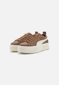 Bruna lädersneakers med en tjock vit platåsula, tydliga snören och en logotyp på sidan. Har rundad tå och texturerade detaljer.