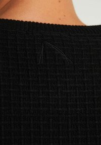 Indumento in maglia nera con un motivo testurizzato. Presenta un collo a coste e un dettaglio con filo allentato visibile sul retro.