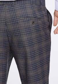 Pantaloni in misto lana con un motivo a quadri in tonalità di marrone e blu. Presentano una tasca sul retro con bottone e una vestibilità sartoriale.