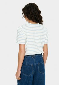 Tricou alb cu dungi albastre deschise, mâneci scurte și puffate, și decolteu rotund. Asortat cu o pereche de pantaloni din denim albastru largi, cu buzunare la spate.