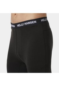 Černé legíny s měkkou texturou, s černým pasem označeným "HELLY HANSEN" bílým písmem. Těsně přiléhající s hladkým povrchem.