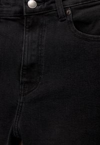 Jeans en denim noir en gros plan montrant la poche avant, la passants de ceinture, le bouton argenté et les détails de couture.